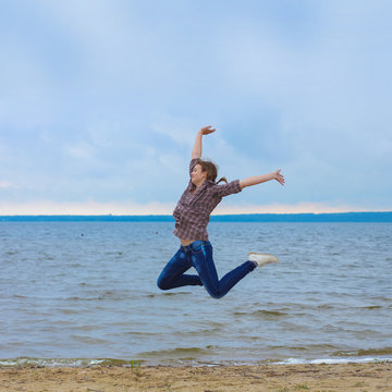 cheerful teen girl jumping on the beach in cloudy windy weather