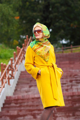 trendy Beautiful senior woman in a yellow coat walks in the park