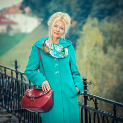 Beautiful mature blonde in  coat posing in the park. Portrait of a senior woman outdoors.