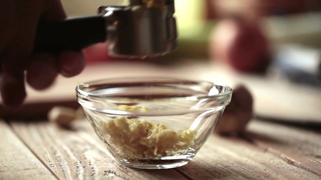 Chef squeezing garlic cloves using garlic press; close up; 