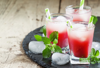 Cold red cocktail with ice and mint on a dark background, select