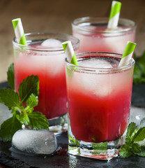 Cold red cocktail with ice and mint on a dark background, select