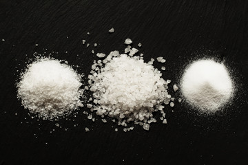 Three types of salt on dark stone background, selective focus