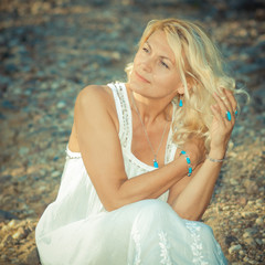 romantic portrait of a beautiful older woman. Mature beautiful blonde in a white dress walks on the  road