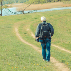 Elderly man travels in wildlife. Portrait of the gray-haired traveler in background of the landscape. Old photographer enjoys traveling and photography