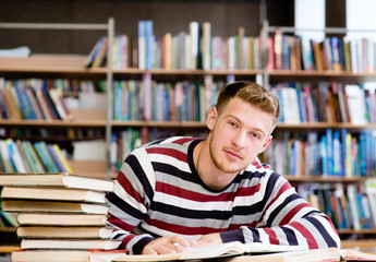 Smiling male student with open book working in a library