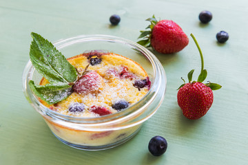 French clafoutis with blueberries and strawberries in ramekins on napkin and  turquoise wooden background