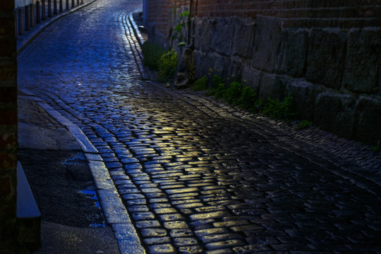 Fototapeta street with wet cobblestones at night in an old town