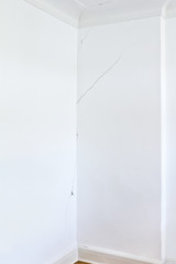 White wall of a room in an old house with a long crack or rip, structural damage.