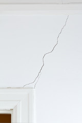 White wall and door case in an old house with a long crack or rip, structural damage.