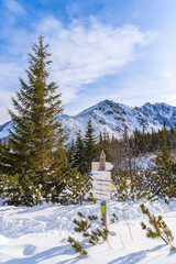 Mountain trail sign in Gasienicowa valley with peaks covered with snow in distance, Tatra Mountains, Poland