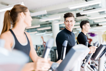 Handsome man and beautiful young woman using a stepper in a gym