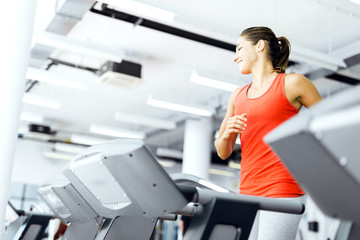 Beautiful young woman running on a treadmill in gym