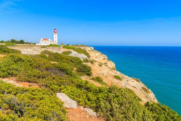 Fototapeta na wymiar Lighthouse building and blue ocean on coast of Portugal near Carvoeiro town, Algarve region