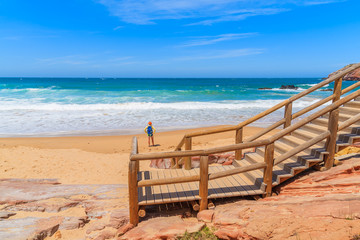 Walkway to Praia do Amado beach and young woman tourist standing in distance, Algarve region, Portugal