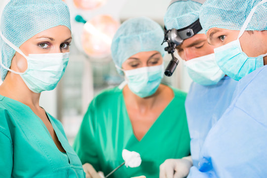 Krankenhaus - &Auml;rzteteam im OP einer Klinik operiert einen Patienten, vielleicht ist es ein Notfall, eine Assistentin oder Assistenzarzt reicht eine Tupferzange