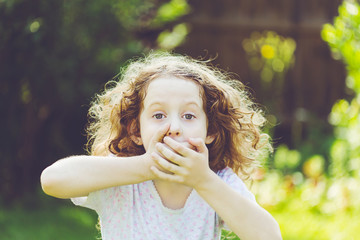 Little girl covering her mouth with her hands. Surprised or scared.