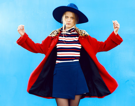 Fashion model in red coat and blue hat poses outdoors