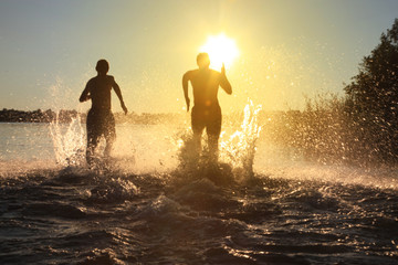 Fototapeta premium Glückliche junge Menschen laufen und springen am See beim Sonnenuntergang