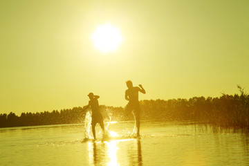 Fototapeta premium Glückliche junge Menschen laufen und springen am See beim Sonnenuntergang