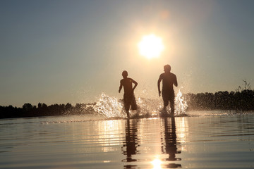 Glückliche junge Menschen laufen und springen am See beim Sonnenuntergang