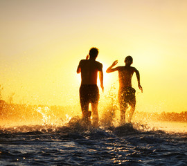 Glückliche junge Menschen laufen und springen am See beim Sonnenuntergang