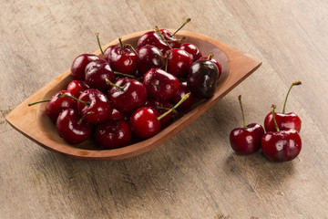 A wooden pot full of cherries over a wooden surface