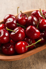 A wooden pot full of cherries over a wooden surface