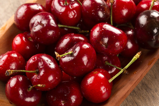 A wooden pot full of cherries over a wooden surface