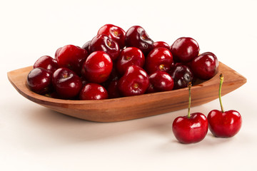 A wooden pot full of cherries over a wooden surface