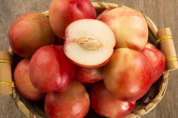 Some peaches in a basket over a wooden surface on a green and na
