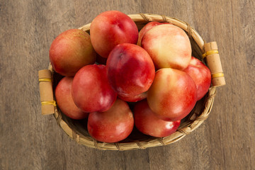 Some peaches in a basket over a wooden surface on a green and na
