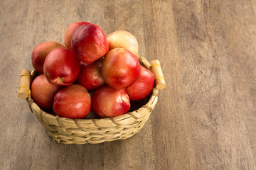 Some peaches in a basket over a wooden surface on a green and na