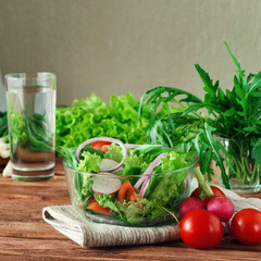 Fresh salad vegetables in a deep bowl of glass. Arugula, lettuce, radishes, onions, cherry tomatoes. concept of a healthy lifestyle. copy space. Free space for text. close up. Square frame