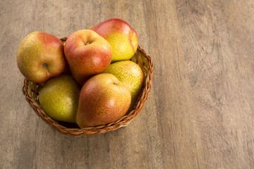 Some pears in a basket over a wooden surface seen from above