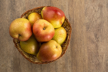 Some pears in a basket over a wooden surface seen from above