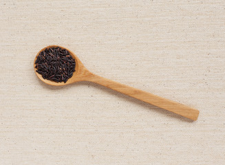 Black rice in wooden spoon with space on canvas background
