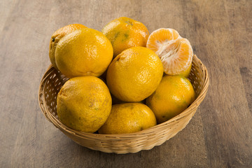 Some tangerines in a basket over a wooden surface