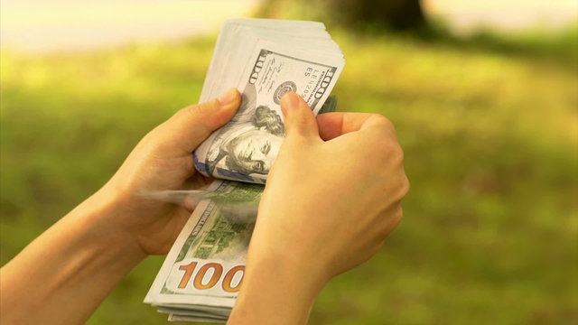 Person counting stack of 100 dollar bills outside
