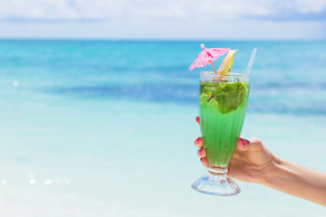 Woman holding glass of fresh mojito cocktail on the beach