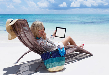 Woman relaxing on the beach and listening to music on iPad