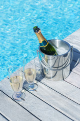 Vertical photo of champagne bottle in bucket and two glasses of champagne on the deck by the swimming pool