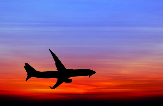 Silhouetted commercial airplane flying at sunset © Satit _Srihin