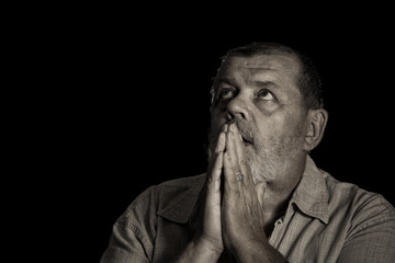 Very emotional sepia toned image of a praying senior man looking up
