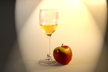 The glass of the white wine and the red apple