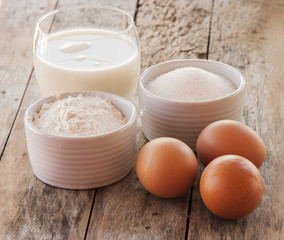 Ingredients for pancakes - eggs, flour, milk on wooden background.