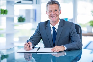 Fototapeta premium Businessman writing on clipboard and looking at camera 