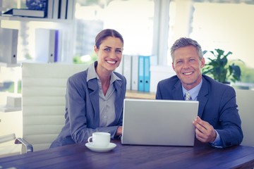 Business people looking at camera and using laptop 