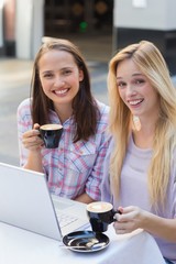 Two happy women friends looking at camera with cup of coffee