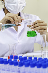 chemist purring blue liquid from flask to a green liquid beaker